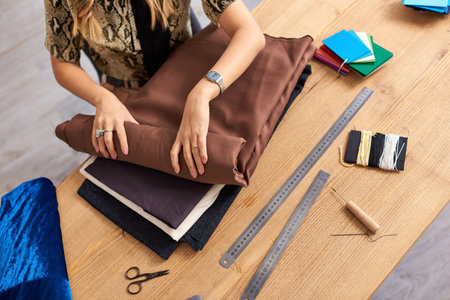 cropped view of clothes stylist checking fabrics samples near sewing supplies in fashion atelier