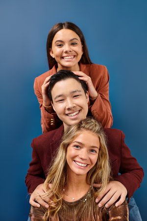 happy diverse teenage friends in stylish clothes posing together on blue backdrop, friendship day