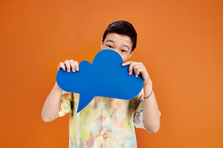 jolly teenage asian boy in everyday vivid outfit looking at camera with thought bubble in hands