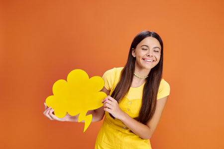 cheerful pretty teenage girl in  vibrant attire holding thought bubble and smiling happily