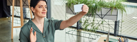 attractive businesswoman in casual attire waving at phone camera during video call, banner