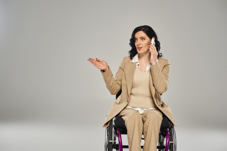 confident good looking disabled woman in pastel suit in wheelchair talking by mobile phone