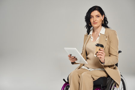 attractive disabled woman in pastel attire in wheelchair with coffee and tablet looking at camera