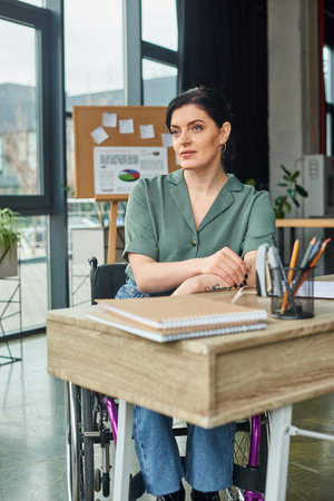 good looking confident businesswoman in wheelchair looking away while working hard in her officeの写真素材