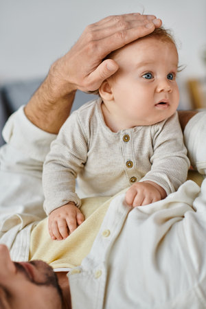 single father with curly hair and beard stroking hair of his infant boy in bedroom, love and care