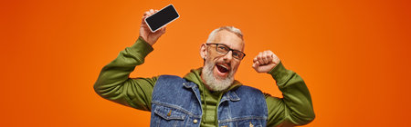 jolly handsome mature man in green hoodie and denim vest holding phone and looking at camera, banner