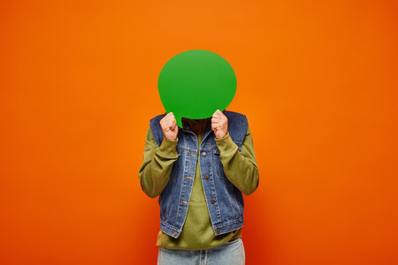 mature male model in fashionable vibrant clothing holding green speech bubble in front of his faceの写真素材