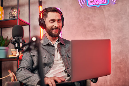 good looking bearded man in comfy everyday attire sitting with laptop during podcast in studio