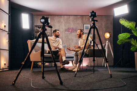 cheerful stylish men with dapper style sitting and discussing interview questions in studioの写真素材