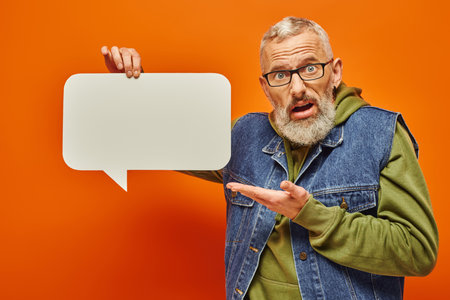 confused attractive mature man in fashionable vest holding speech bubble and looking at camera