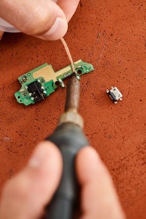 cropped view of repair specialist soldering electronic microscheme in workshop, small businessの写真素材