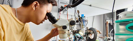 experienced asian repairman looking in microscope and testing electronic devices, side view, banner