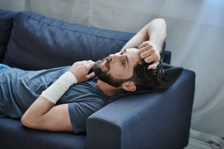 desperate man with bandage on arm after attempting suicide lying on sofa, mental health awareness
