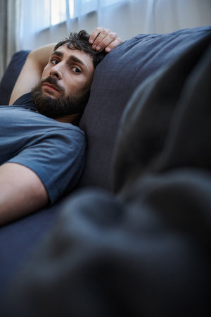 depressed hopeless man in cozy home wear lying on sofa during mental breakdown, psychotherapyの写真素材