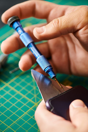 partial view of technician opening smartphone with screwdriver during testing in own workshop