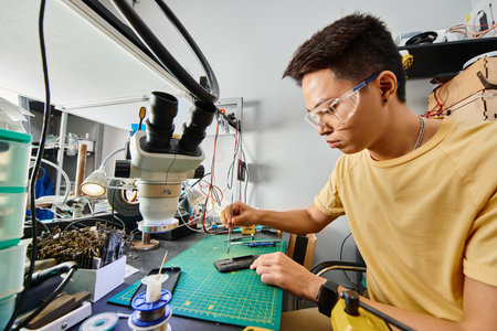 concentrated asian repairman in goggles making technical expertise of mobile phone in repair shop