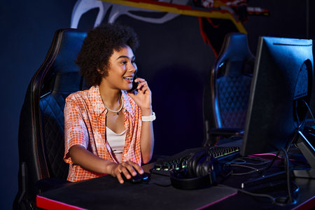 happy black woman sits at her computer and having phone call near computer, cybersport club