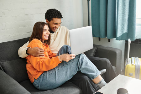 diverse couple snuggle on couch with their faces illuminated by the glow of the laptop screen, movieの写真素材