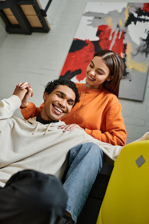 happy woman holding hands with her african american boyfriend near luggage in hostel room