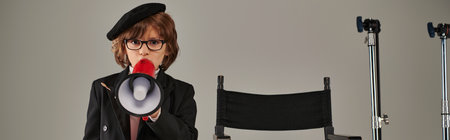 filmmaker kid stands confidently before director chair and speaking in megaphone on grey, bannerの写真素材