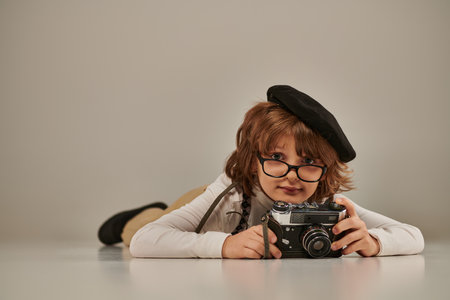 happy young photographer in beret and suspenders taking photo on retro camera and lying on floorの写真素材