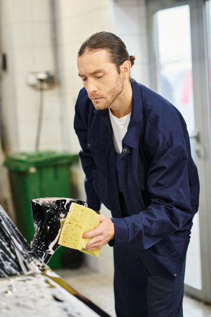 good looking hard working specialist with collected hair in uniform washing car with soapy spongeの写真素材