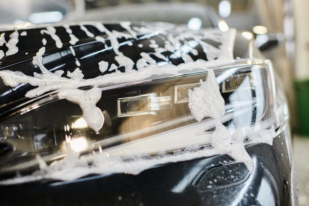object photo of headlight of black modern car covered with soap during washing service in garageの写真素材