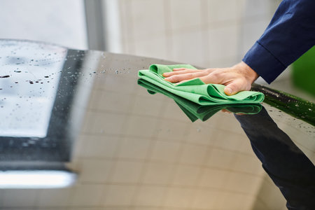 cropped view of devoted professional worker in uniform using rag to clean black modern car in garageの写真素材