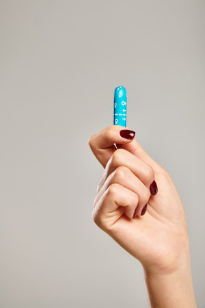 object photo of hygienic tampon in hand of unknown woman with nail polish on gray backgroundの写真素材