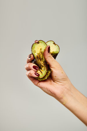 unknown female model with nail polish squeezing fresh green avocado in her hand on gray backdropの写真素材