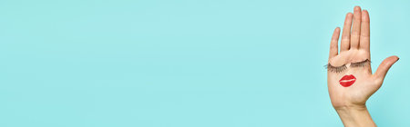 artificial eyelashes and lipstick in form of face on palm of unknown woman on blue backdrop, bannerの写真素材