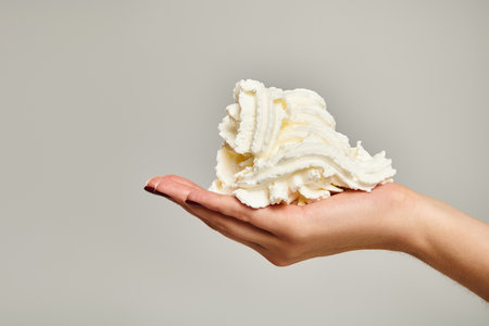 object photo of sweet delicious whipped cream in hand of unknown young woman on gray backdropの写真素材