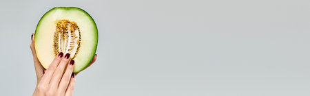 unknown woman with nail polish picking up seeds from fresh cantaloupe on gray backdrop, bannerの写真素材