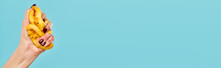 unknown woman with nail polish squeezing juicy persimmon in her hand on blue background, bannerの写真素材