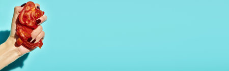 unknown woman squeezing two parts of red fresh juicy tomato on vibrant blue background, banner