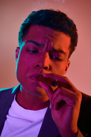 portrait of young african american man with cigar in mouth on pink background with blue lightingの写真素材