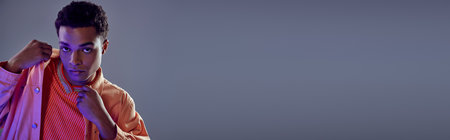 banner of handsome african american guy in peach shirt looking at camera on grey with blue lightの写真素材