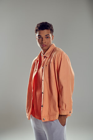 stylish man in peach shirt standing against grey wall, showcasing his impeccable fashion sense