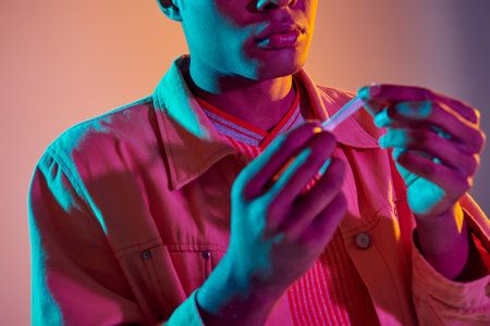 cropped african american guy holding rolled cigarette on colorful background with blue neon lighting