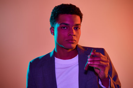 african american guy in blazer holding match with fire and cigar on pink background with lighting