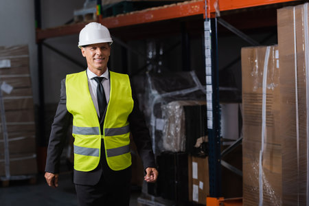 Smiling man in safety vest and hard hat and safety vest walking in warehouse, professional headshotの写真素材