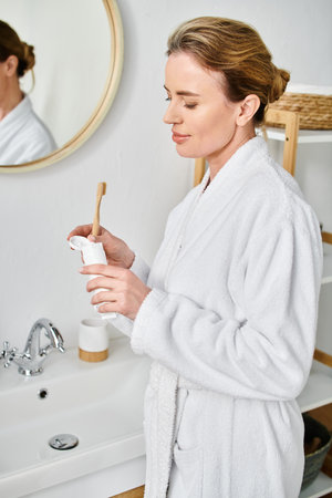 attractive blonde woman with collected hair in bathrobe brushing her teeth in front of mirror