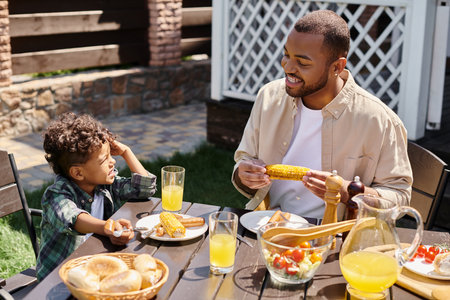happy african american father having family bbq with curly son on backyard of house, grilled cornの写真素材