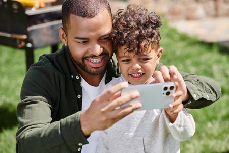 happy african american boy taking selfie on smartphone with his father in braces on backyard