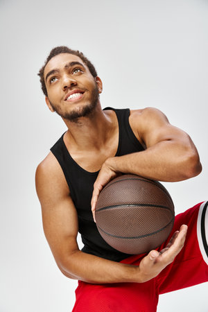 attractive jolly african american man in sportwear posing with basketball on gray background