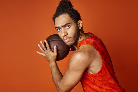 attractive african american man in vivid sport uniform holding basketball and looking at camera