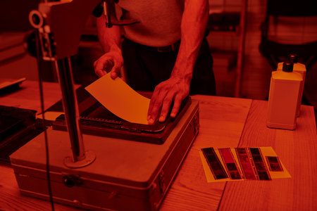 young photographer focuses on delicate process of enlarging film in darkroom with red lightの写真素材