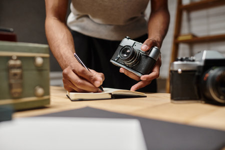 cropped african american guy immersed in writing holding his analog camera in photo studioの写真素材