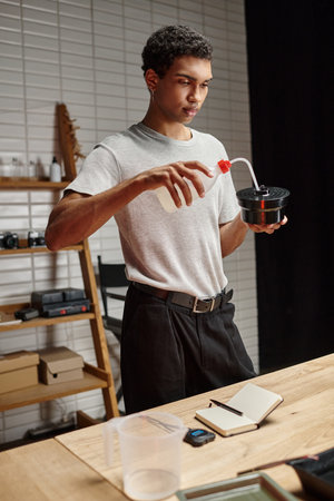 young african american photographer pouring chemical solution into film developing tank