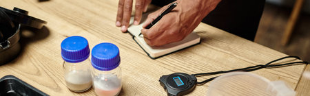 cropped view of african american man taking notes near bottles with film developing powder, banner